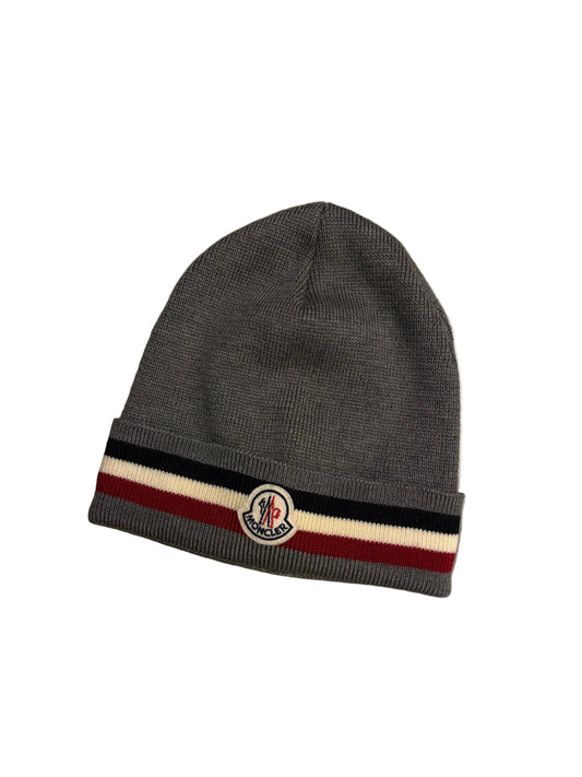 Gray beanie with a striped band and logo on a concrete surface